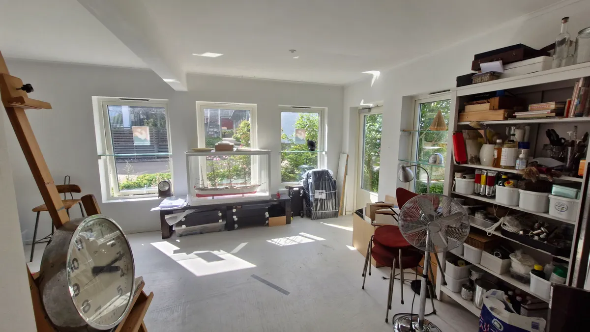 En stor stue med højt loft, fuld af diverse ting og møbler, inklusiv en stålampe og en fan. En stor model af skib er