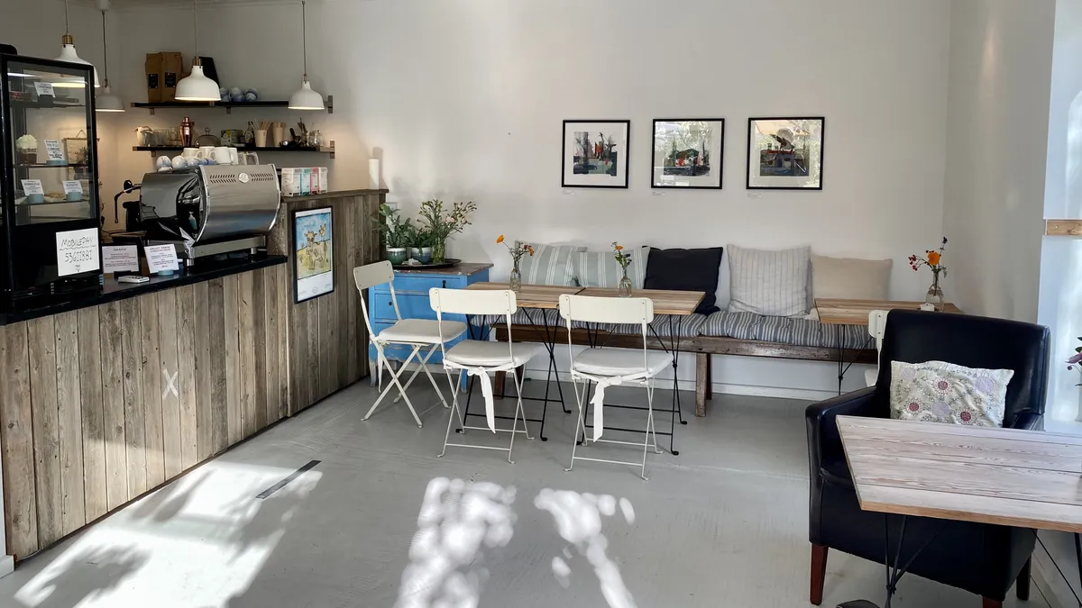 Kaffebar med moderne interiør og smukt dekoreret sofa med tæpper og blomster. Her er også en borde og stole til gæsterne og