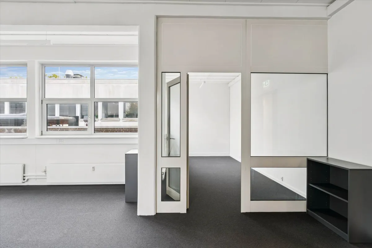 En tom, hvidmalet kontor med store vinduer, spejle og en sort høj hylde, der vender mod højre side