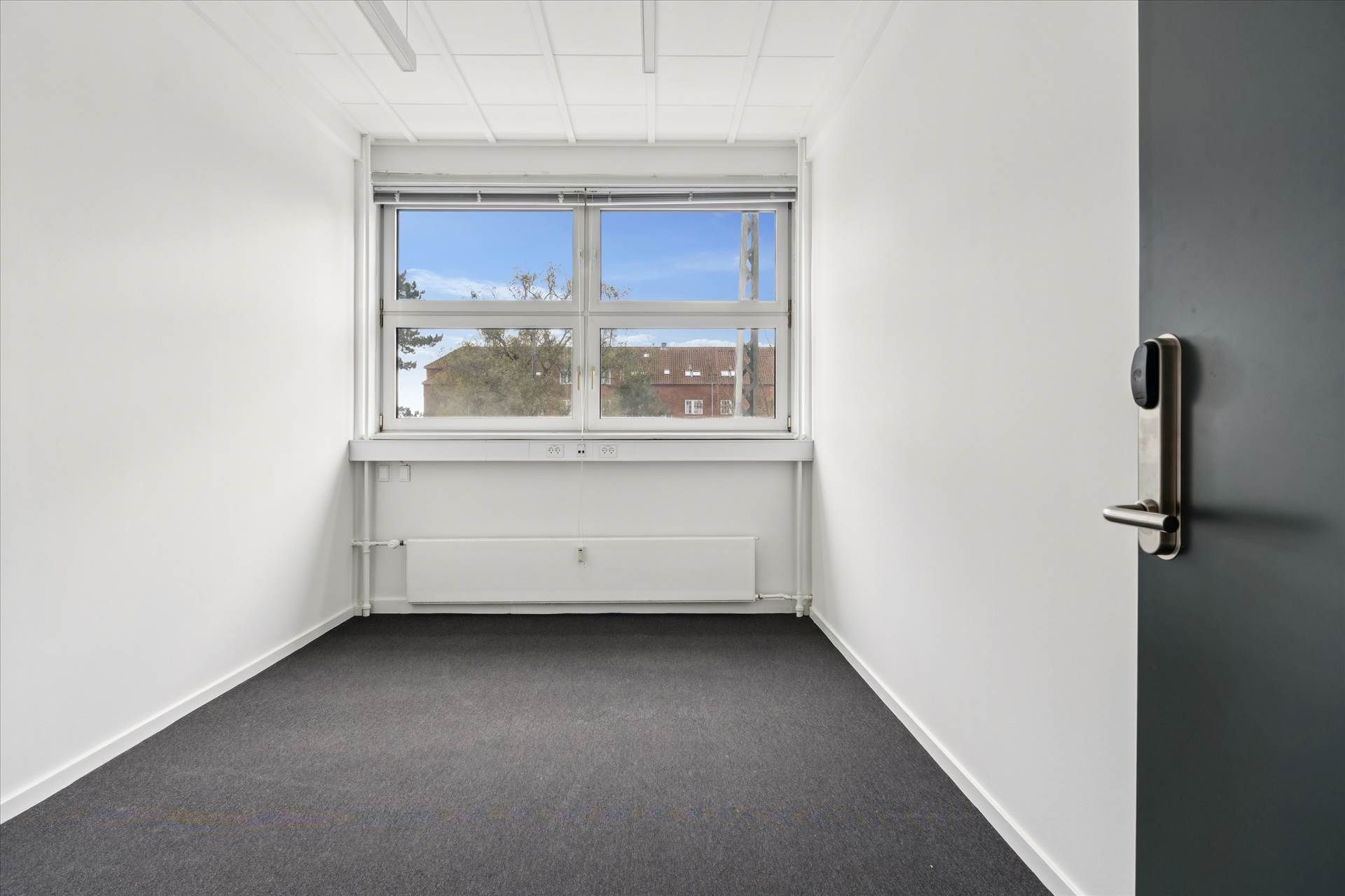 Et ubeboet kontor med høj synlighed og en stor vindue med udsigt til bygninger og træer i baggrunden.