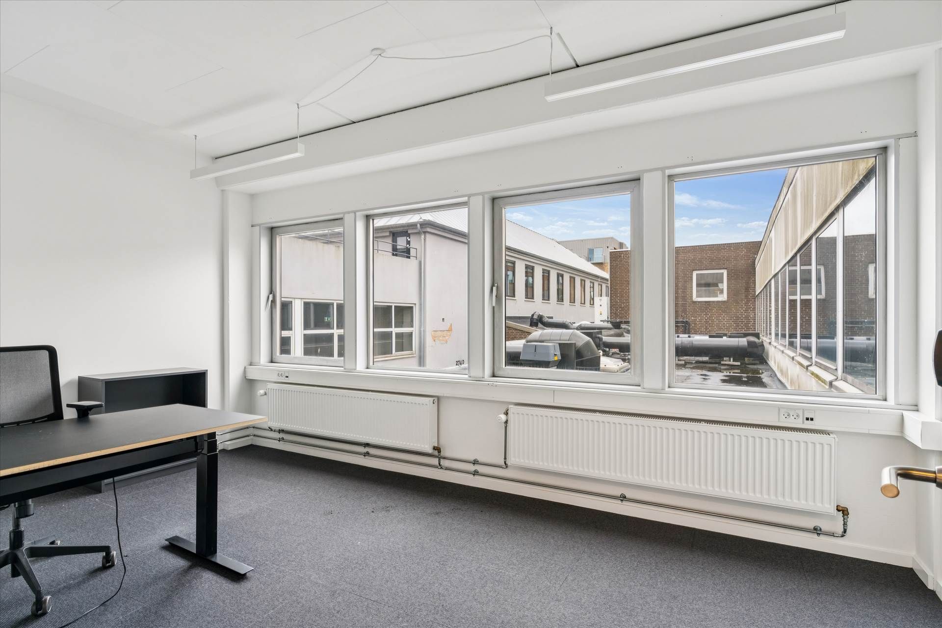 Værelse med skrivebord og kontormøbler samt radiatorer under vinduene og hvide vægge og loft