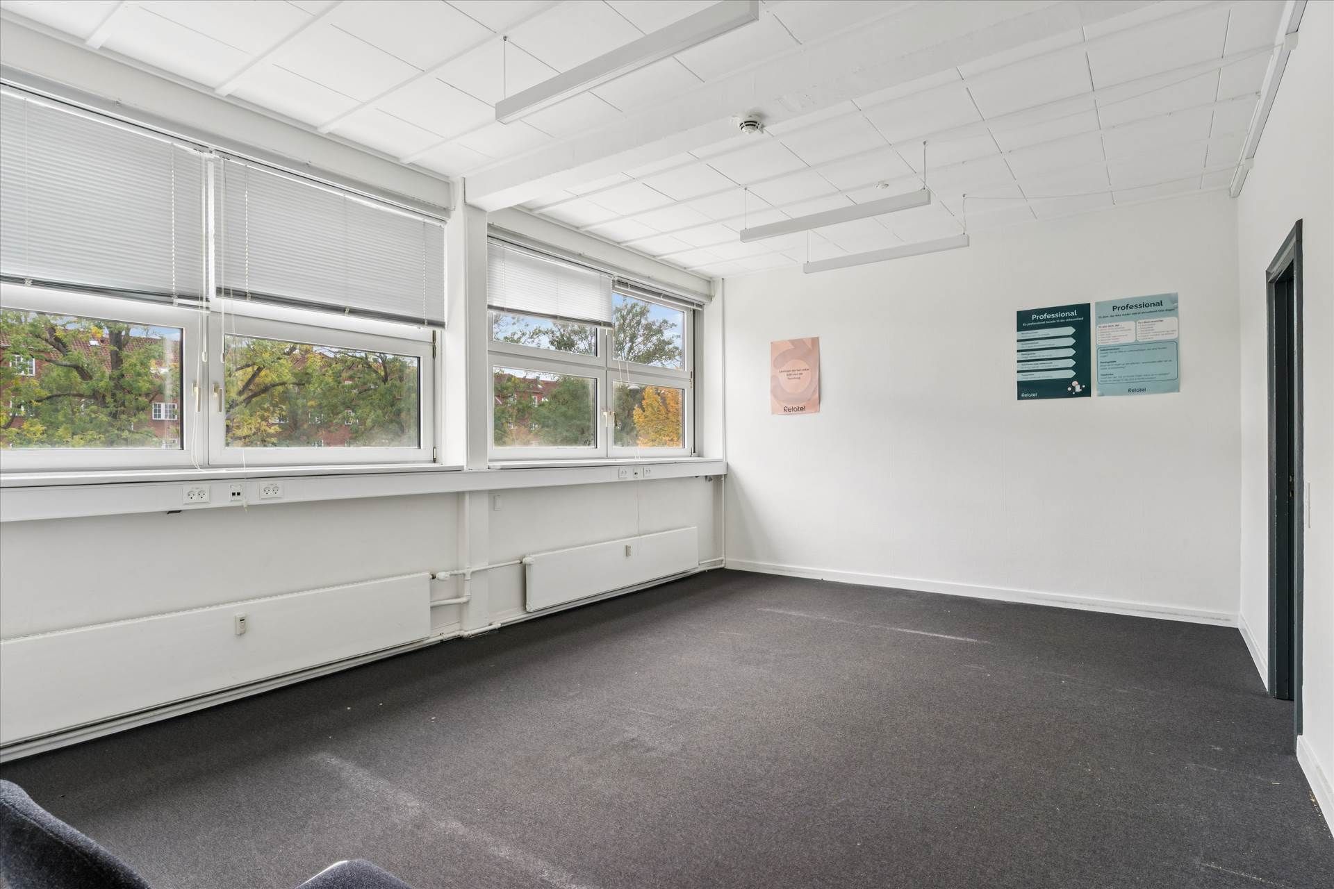 En tom kontorlokal med hvide vægge, vinduer, lysekroner og gulvbelægning med tre stikkontakter ved vinduet