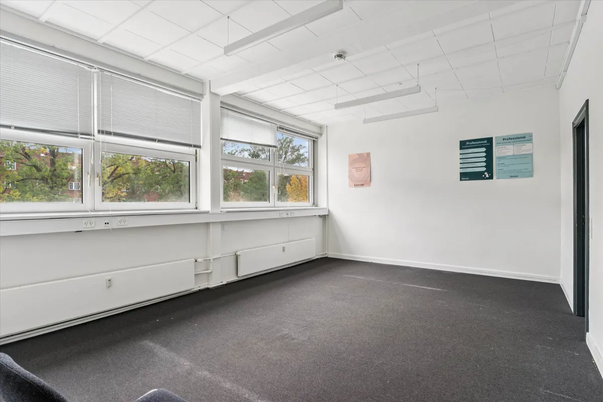 En tom kontorlokal med hvide vægge, vinduer, lysekroner og gulvbelægning med tre stikkontakter ved vinduet