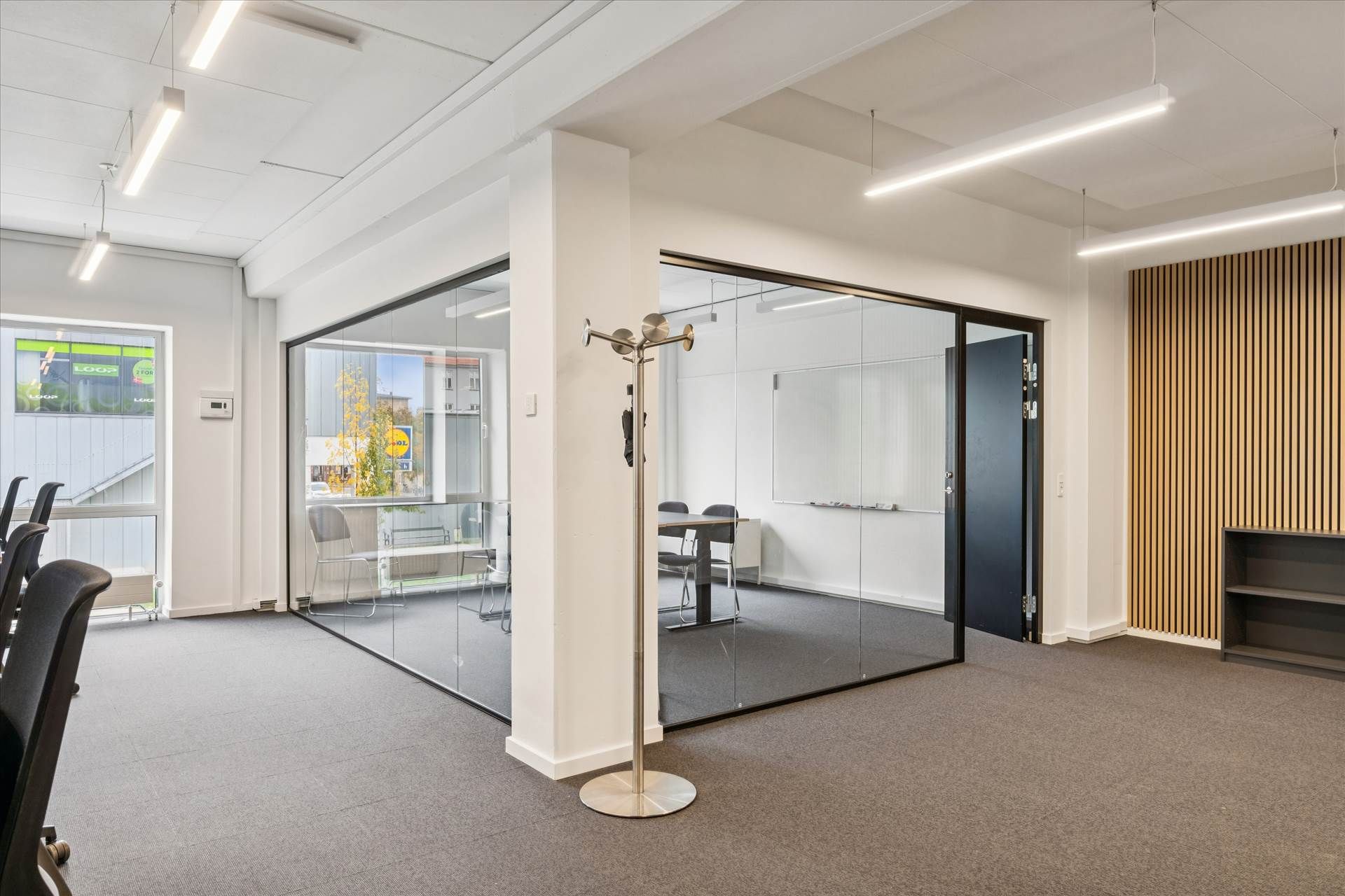 Kontorlokaler med moderne møbler og lyse glasvægge, samt hængende lamper og en hylde med bøger