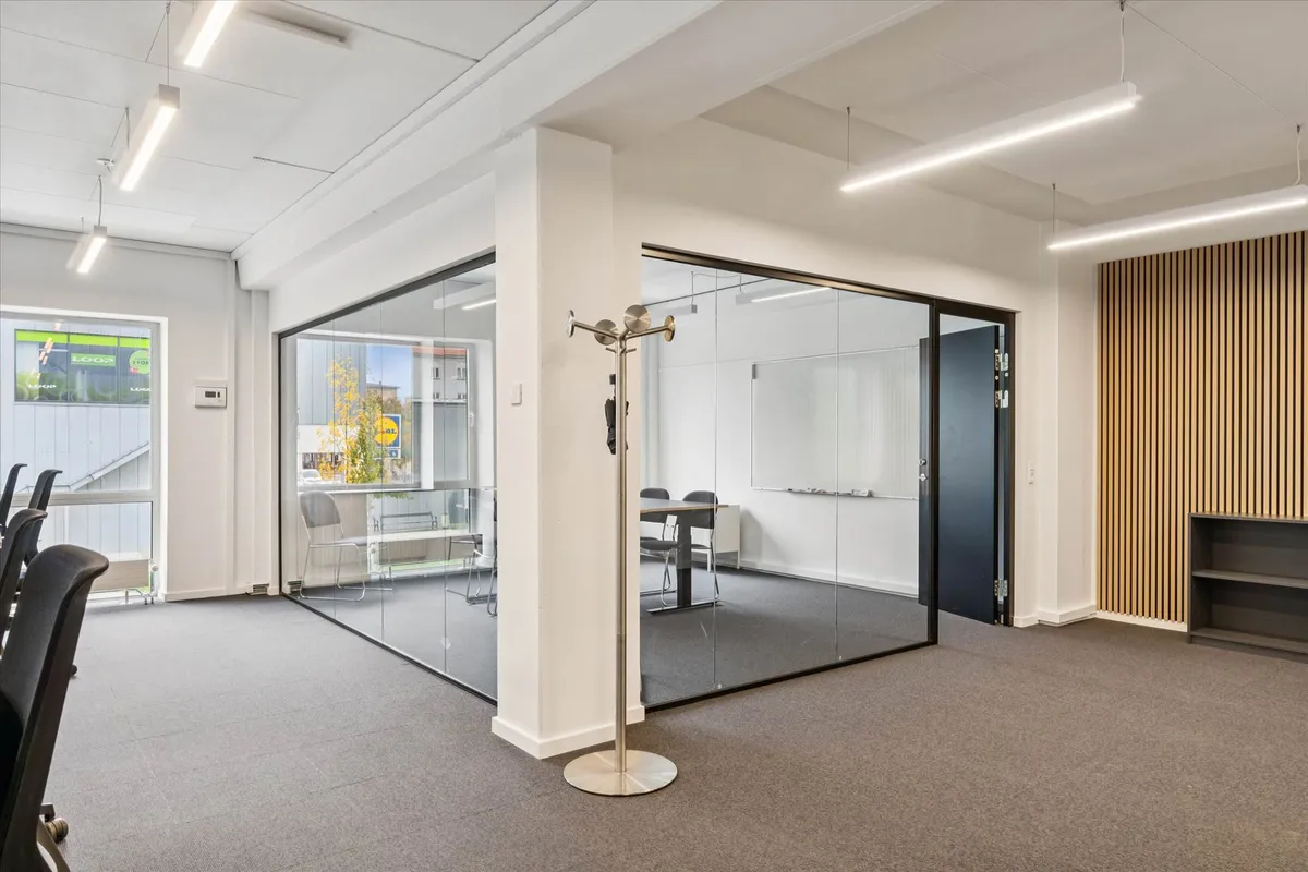 Kontorlokaler med moderne møbler og lyse glasvægge, samt hængende lamper og en hylde med bøger