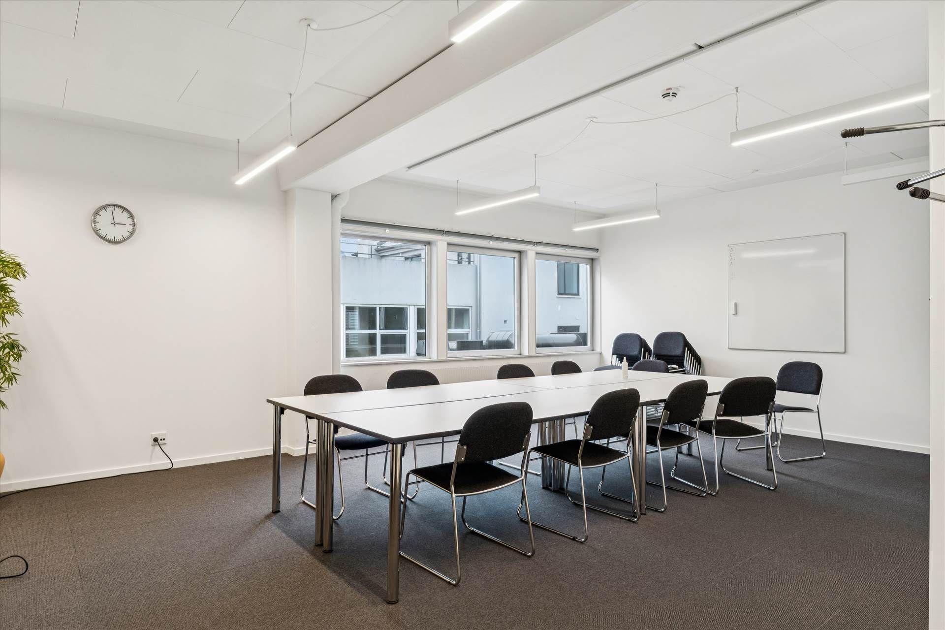 Kontorlokaler med høj synlighed. Store vinduer og hvide vægge. Bord og stole med mødelomme. Lyskroner og en tavle. Tidspunkt
