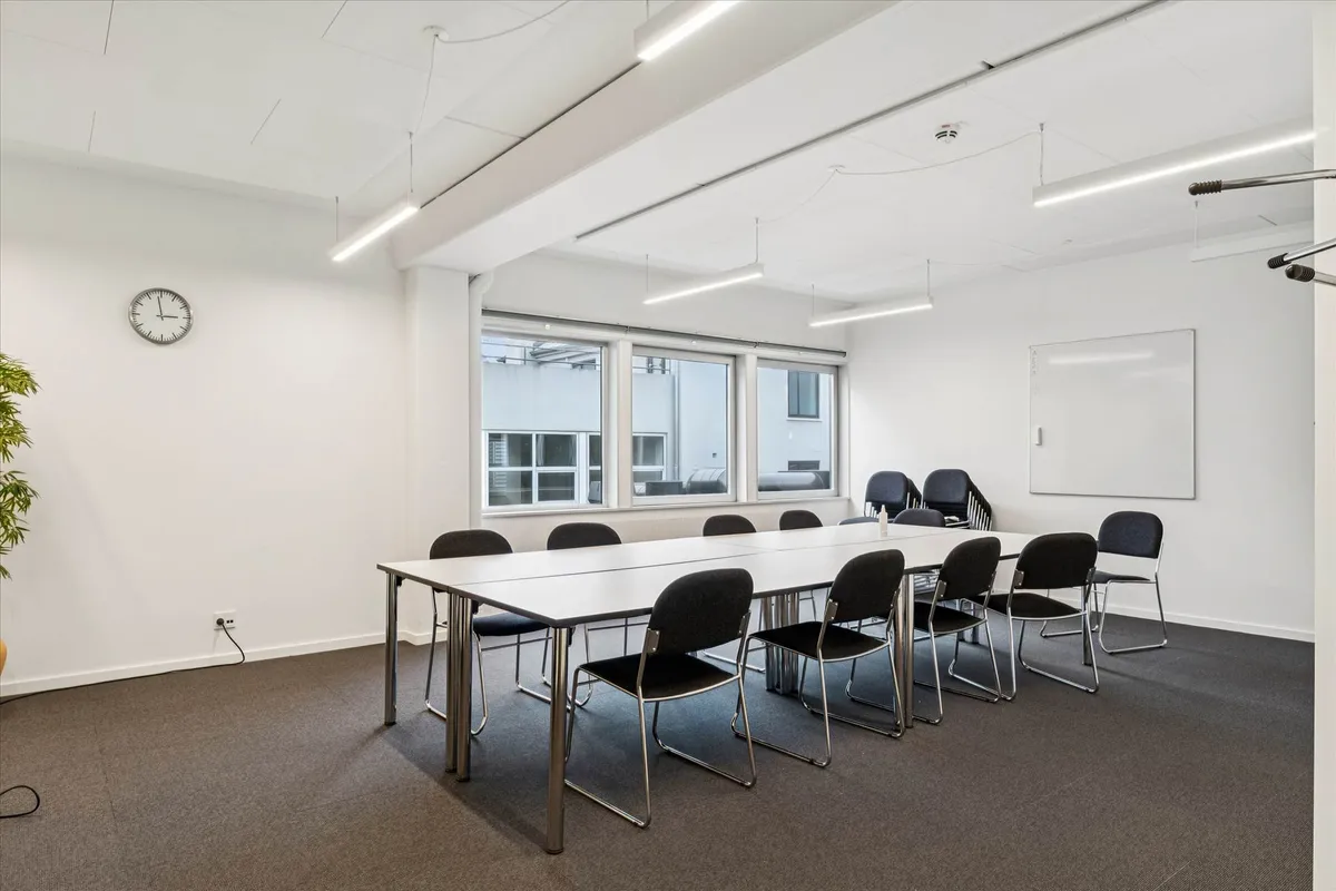 Kontorlokaler med høj synlighed. Store vinduer og hvide vægge. Bord og stole med mødelomme. Lyskroner og en tavle. Tidspunkt