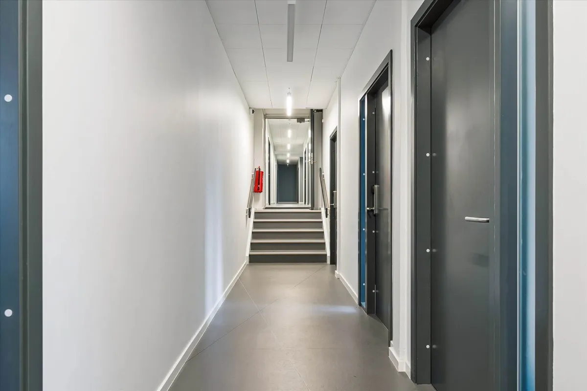 Hallen med lysegul gulvbelægning og hvide vægge og tre døre på højre side samt en trappe i midten