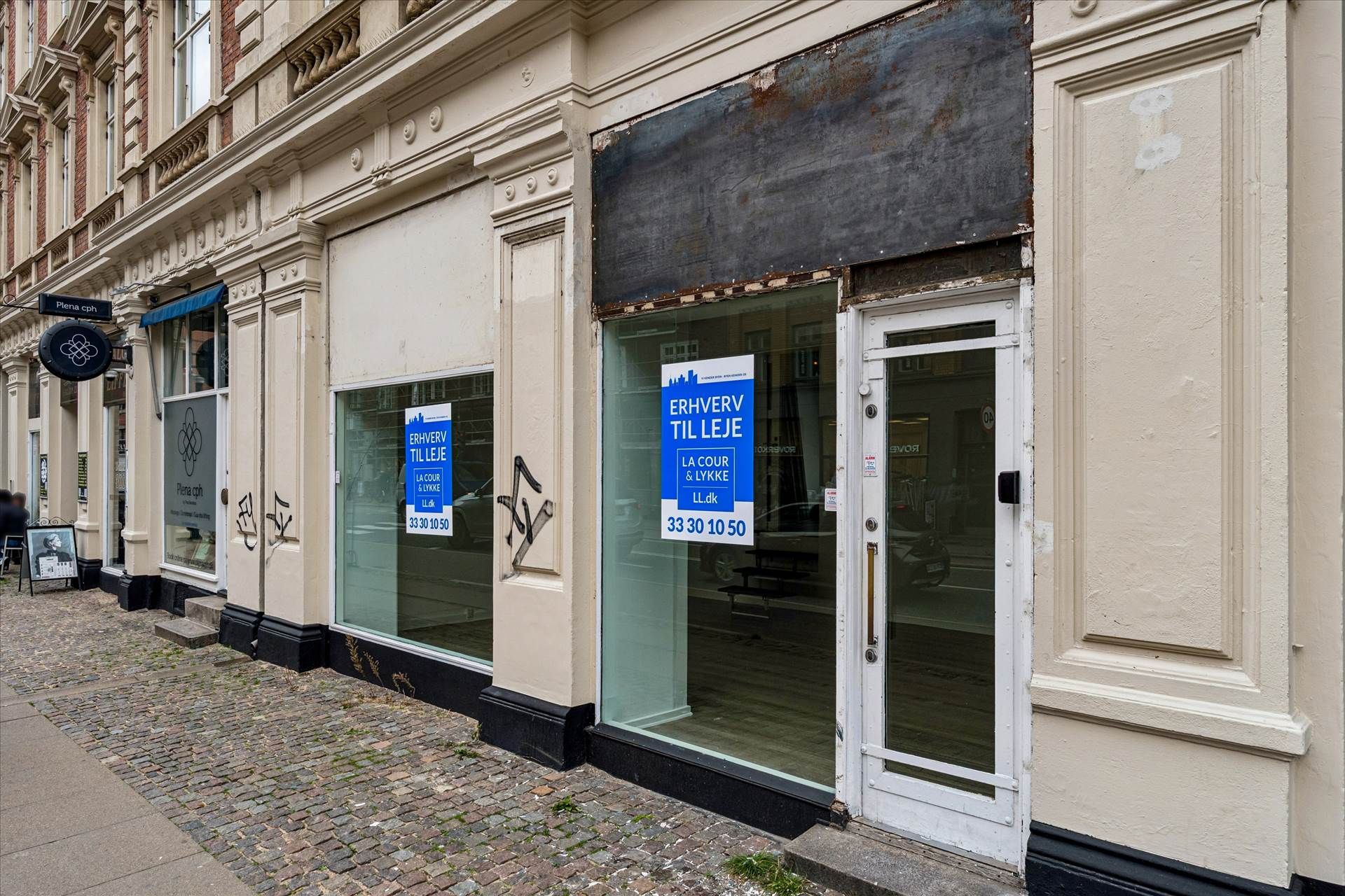 Butikslokal til leje med facade på Amagerbrogade med glasdøre og vinduer med reklameskilte og tydelige åbningstider