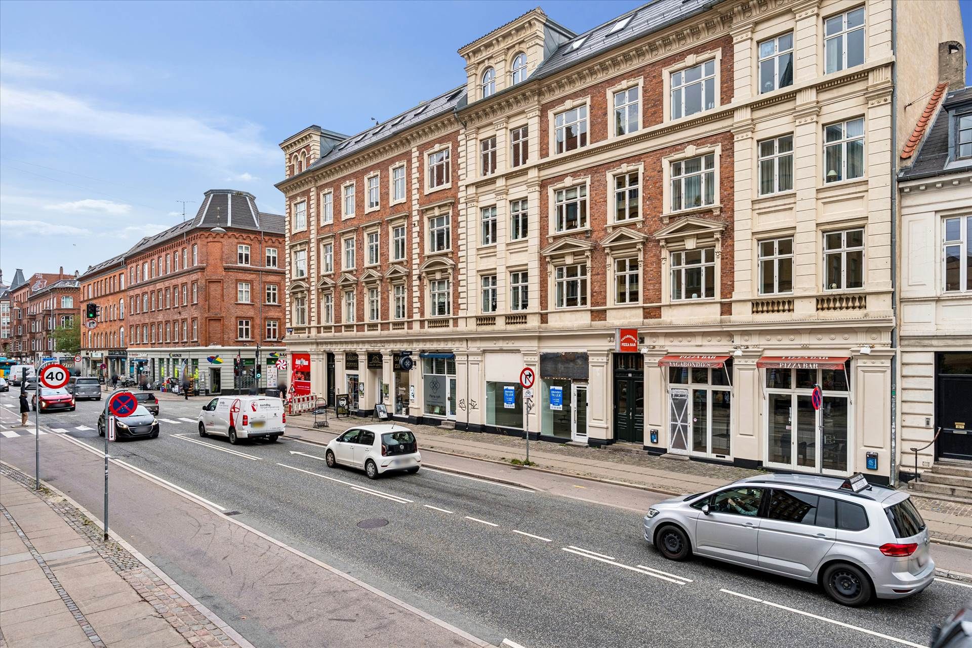 Bygade med højtliggende butikker og store vinduer og en taxivogn, der kører langs vejen