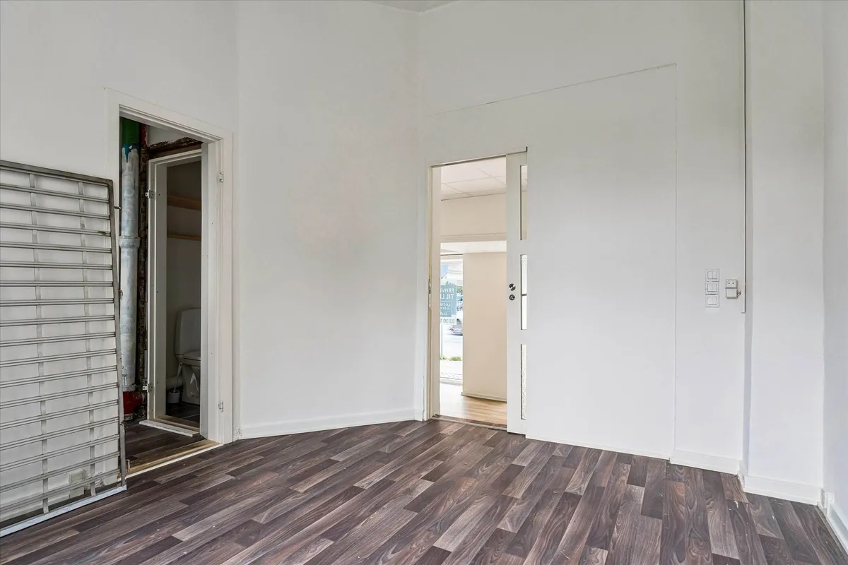 Butikslokale med moderne design og lyse vægge, åben dør til et lille badeværelse og en åben garderobe