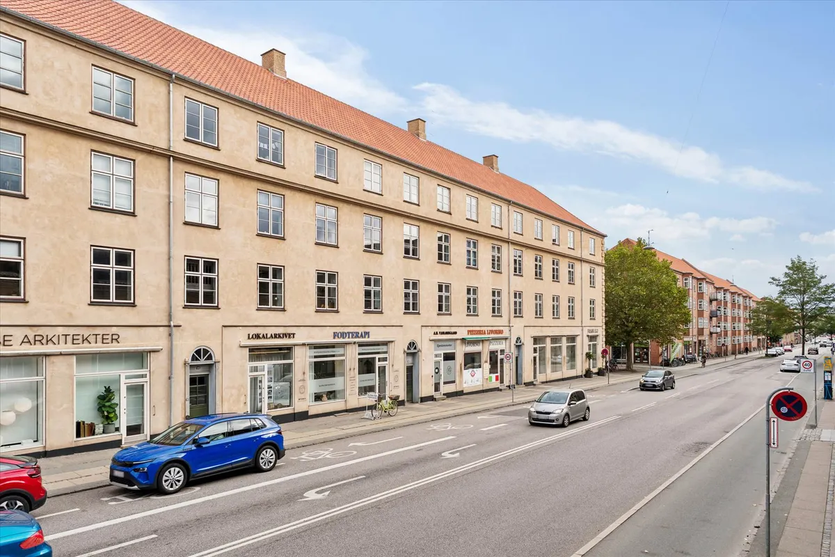 Vanløse med forretningslokaler og biler på vejen, smukke gamle bygninger og flotte træer