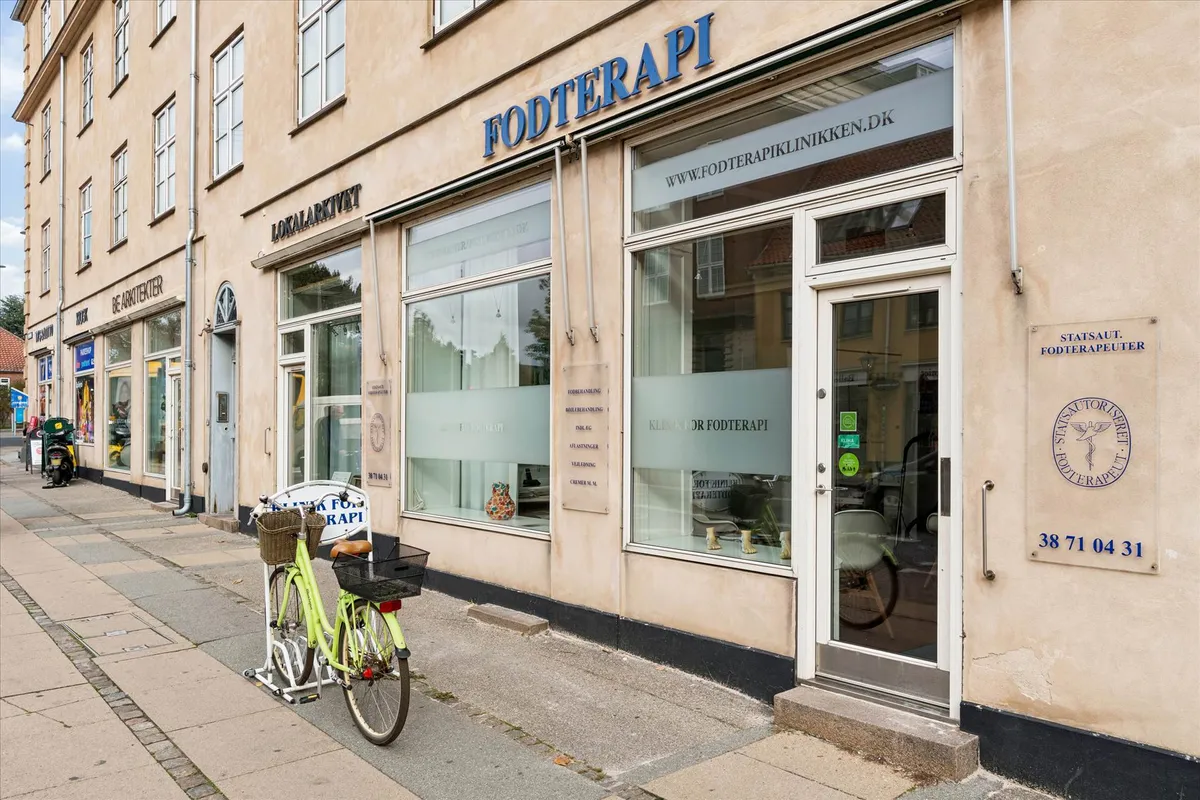 En grøn cykel parkeret foran en butik med navnet Fodterapi og teksten www.fodterapiklinikken.dk