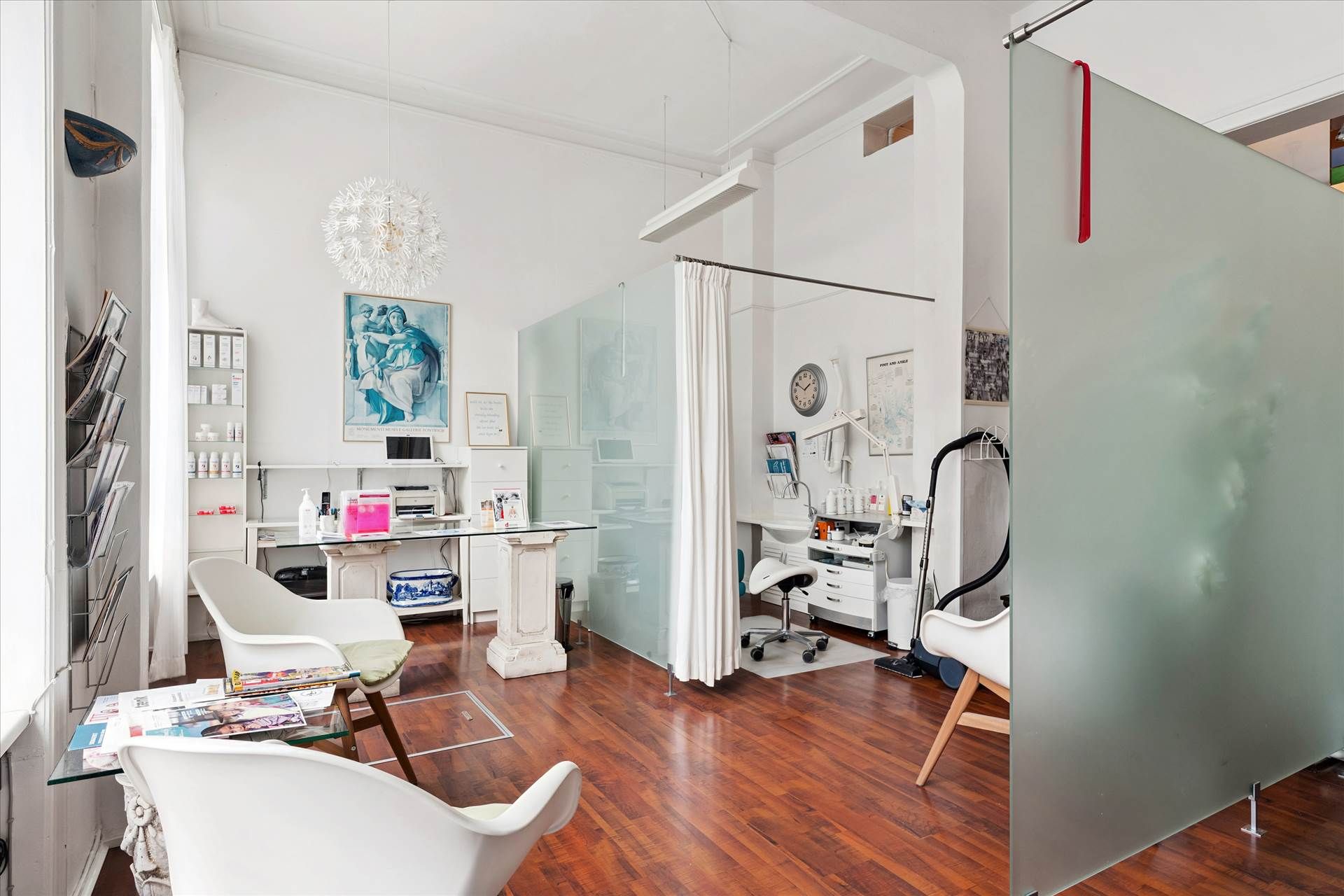 En hvid interiør med hårde trægulve, hvide stole, skrivebord, hylder, loftslampe og en gulvstøvsuger.