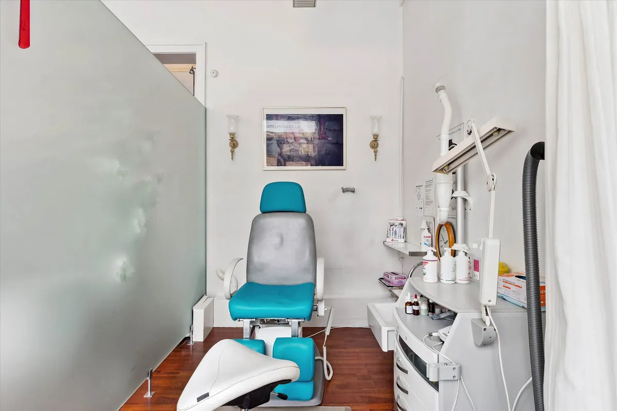 Billede af et lægeværelse med en hvid og blå lægestol og et højt, lyseapparat. Der er også en høj, hvid kommode med flere