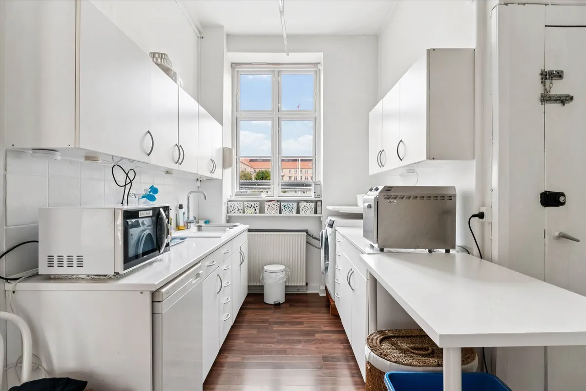 Et rent og velorganiseret køkken med hvide skabe og bordplade samt en mikrobølgeovn og en brødrister placeret på et bord