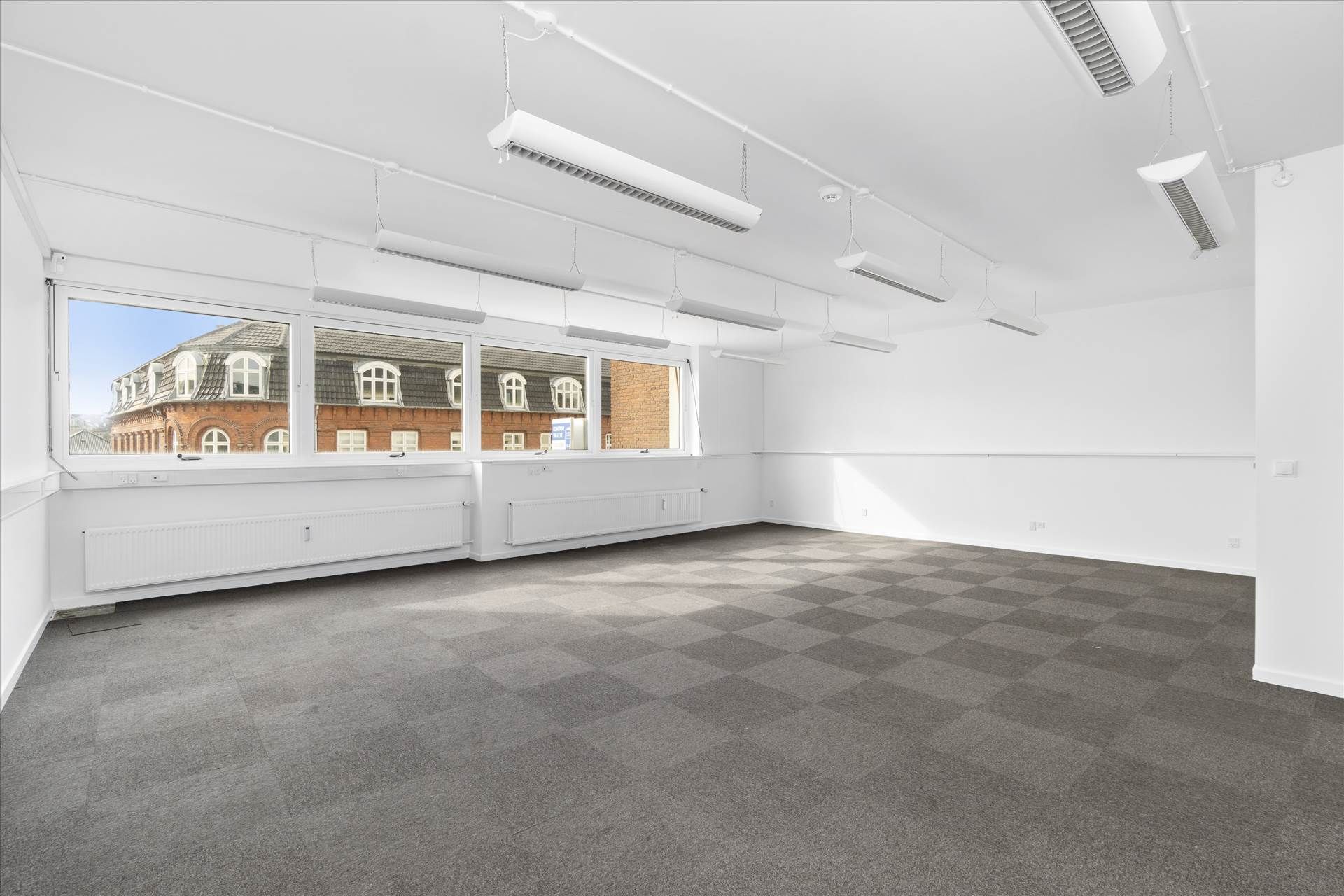 Lukket rum med lysevinduer og gulvtæppe, hvide vægge, luftkanaler og lysekroner med lyspærer. Adgang til elevator og