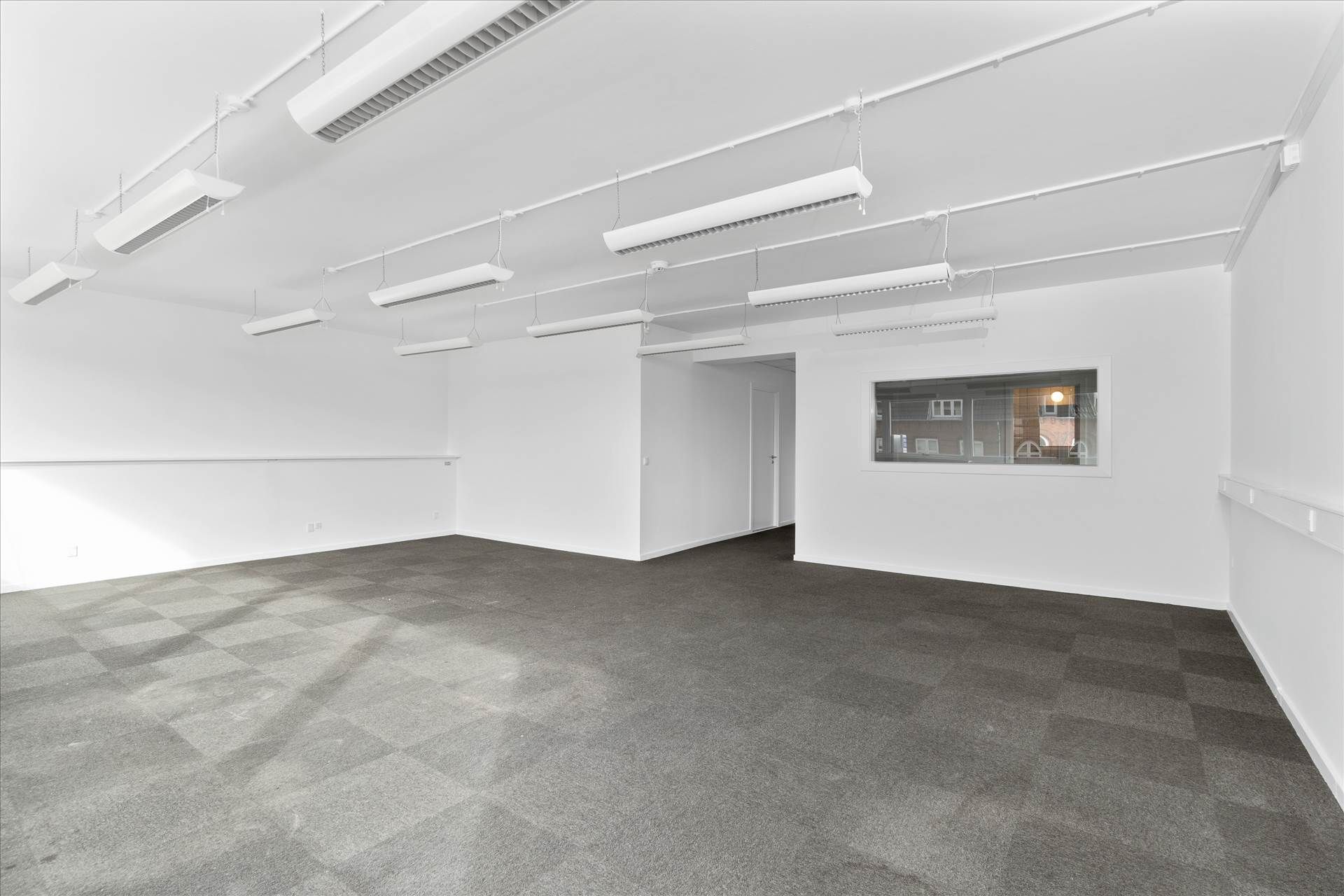 En stor, tom og lys kontorlokation med hvide vægge og mørkegrå gulvbelægning, der ser moderne ud