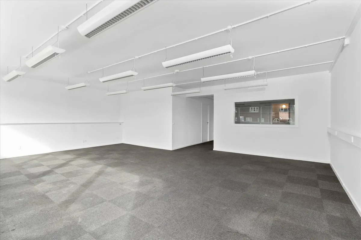 En stor, tom og lys kontorlokation med hvide vægge og mørkegrå gulvbelægning, der ser moderne ud