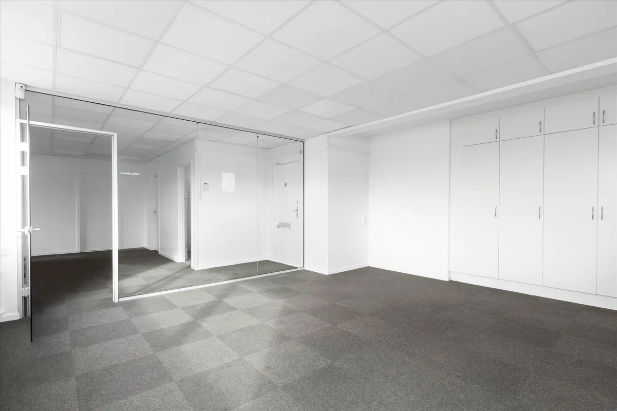 Velindrettet og charmerende kontorrum med hvide vægge og loft, glasdøre og gulvbelægning af grå karper. Værelset er tomt og