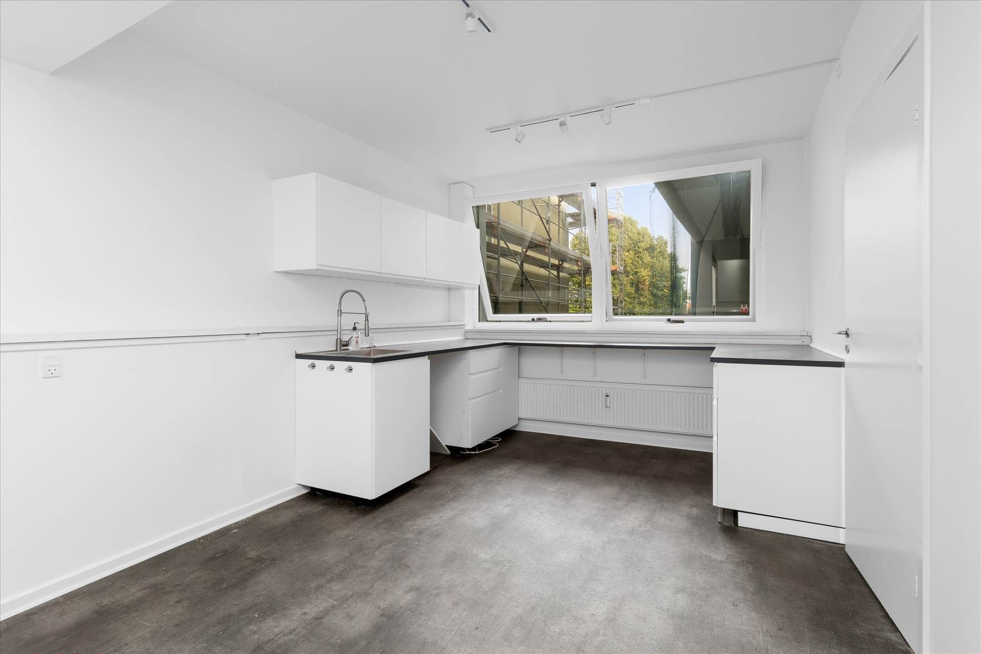 Modernt kontor med hvide vægge, et køkken med en høj skab, en blikfang til vinduet og et hjørne med en radiator