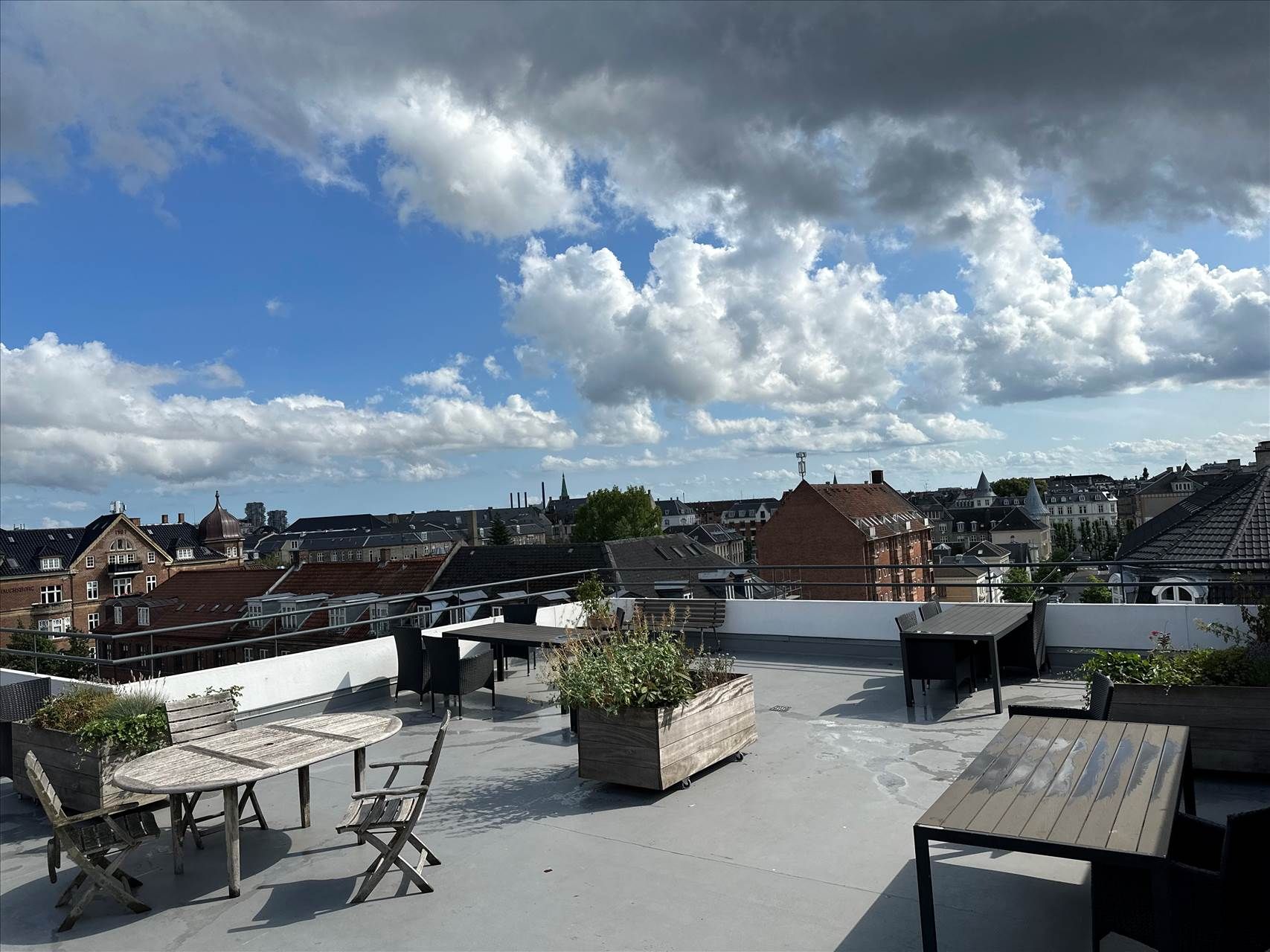 Tagterrasse med udsigt over byen, borde og stole, lyseregn og planter i store kasser