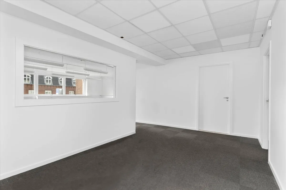 Kontorlokaler med hvidt loft og hvide vægge samt gulvbelægning i sort og hvide og lysegule loftsbelysningslampe