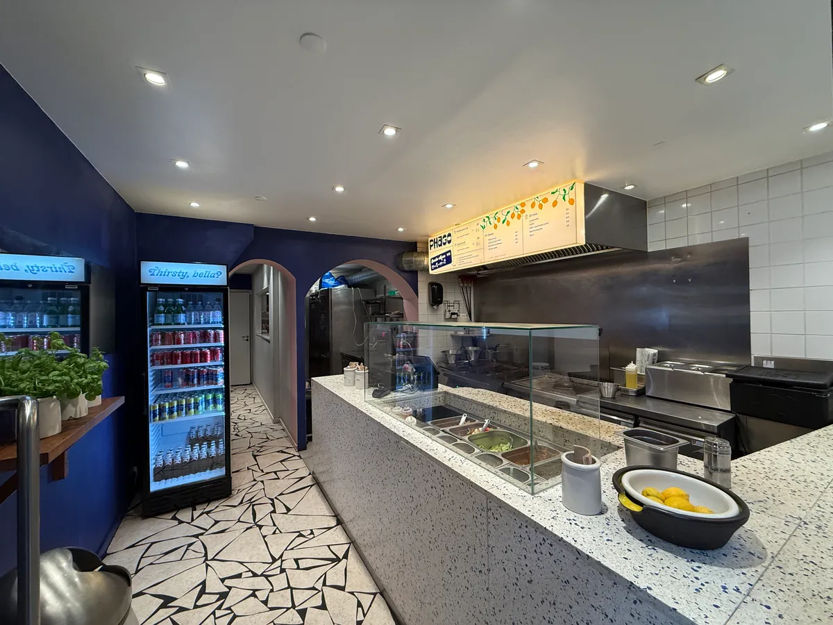 Take-away med køkken og køleskabe med drikkevarer og friske planter på hylden i lyserødt og hvidt interiør