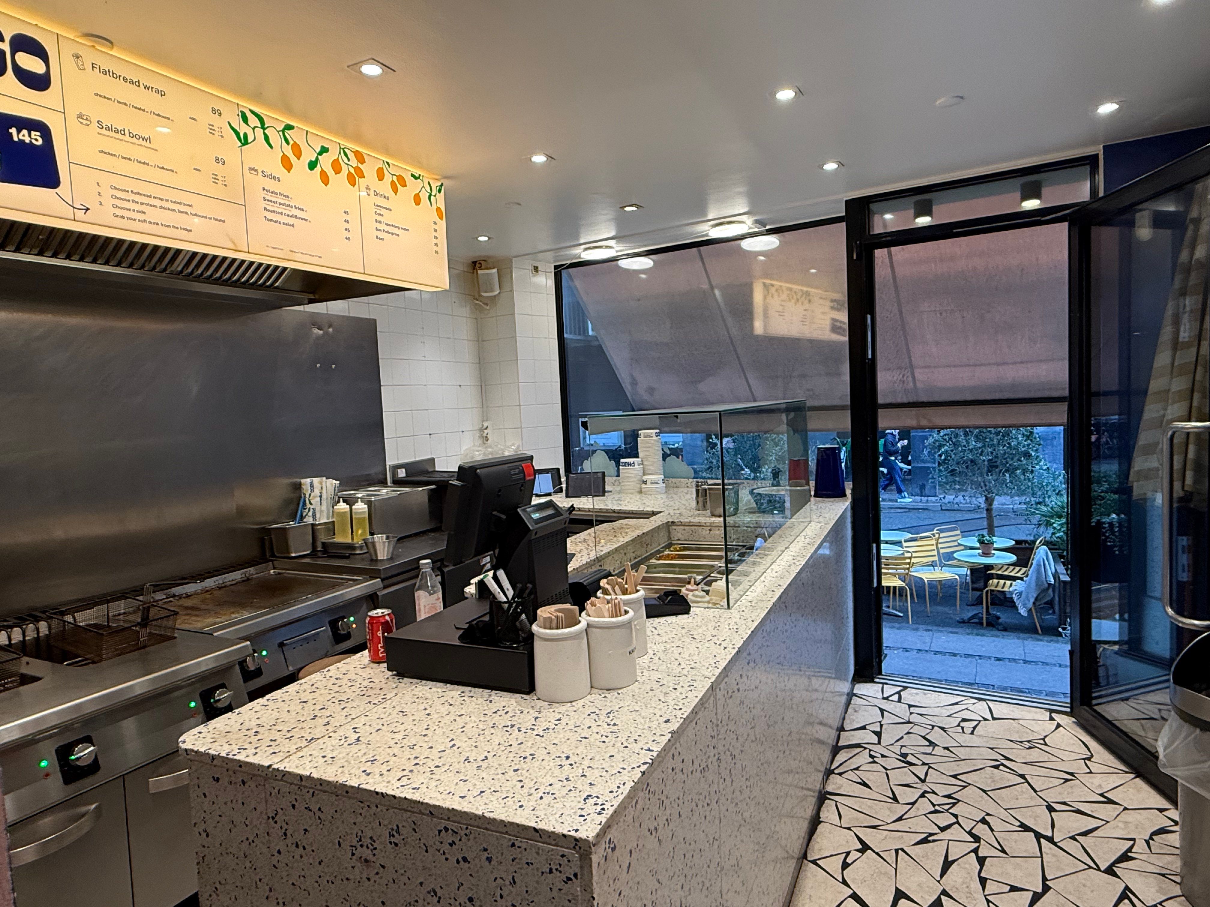 Køkken med moderne udstyr og spisebord udenfor med lyse stole og planter.