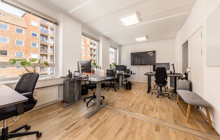 Moderne kontor med lyse gulve og højt loft med lysekroner. Kontorborde med computere og stole i rækker. Vinduer med udsigt