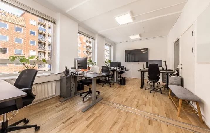 Moderne kontor med lyse gulve og højt loft med lysekroner. Kontorborde med computere og stole i rækker. Vinduer med udsigt