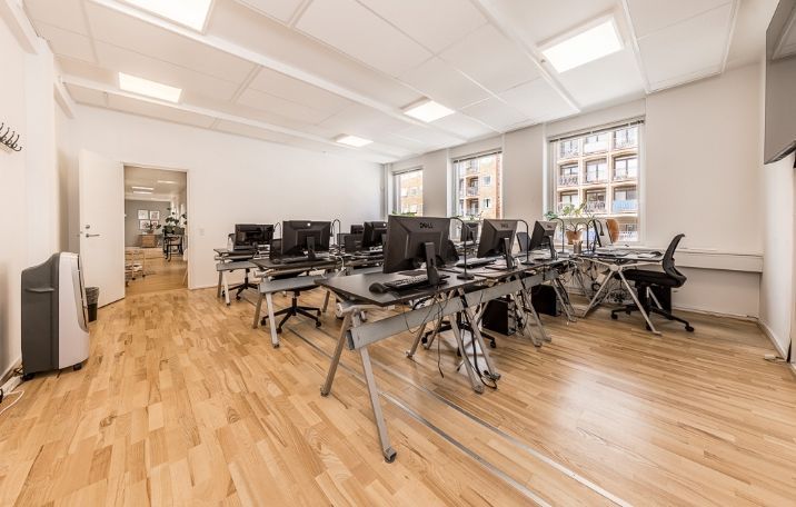 Kontorlejemål med computere og skriveborde i et rum med hårdt trægulv og hvide vægge