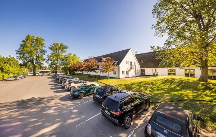 Parkeringsplads med biler og grønt, hyggelig gård og solrig dag med lyse himmel