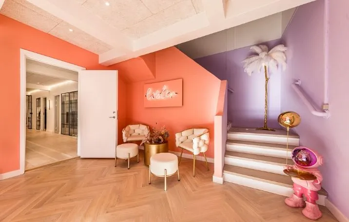 Kontorområde med hvide stole og gulve, gule og orange vægge, en hvid stige og en pink robot på gulvet