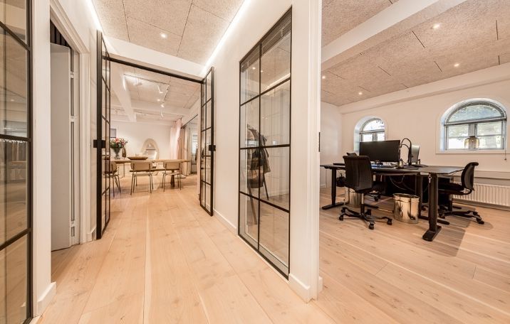 Kontor med lyse gulve, slanke stolpe og glasdøre. Bord med monitor og skrivebordslampe. Højt, halvcirkelformet vindue. Bord