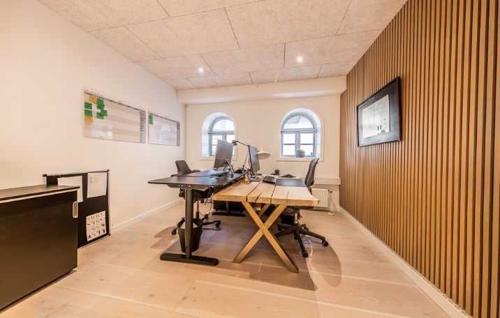 Kontorrum med to skriveborde og stole samt to skærme og lampe samt hængende billede på væggen