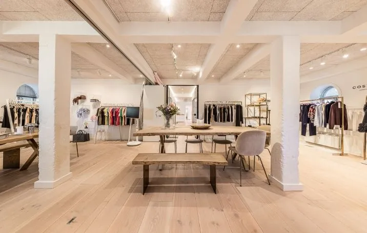 Elegant interiør med massivt trægulv og høje hvide søjler og lofter samt moderne møbler og hængehylder med tøj