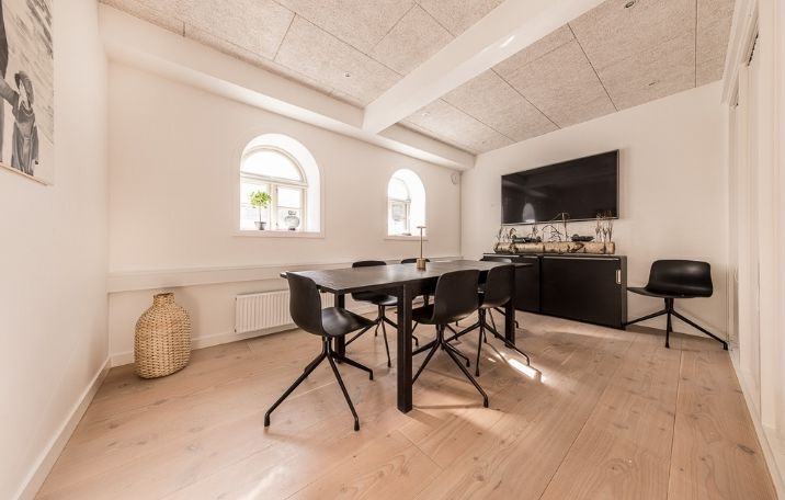 Minimalistisk kontor med højt loft, lyse trægulve og runde vinduer, tv og hyggeligt vinduesbord