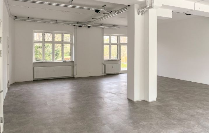 En stor og lys rummeligt lokale med lyse gulvfliser og hvide vægge, hvor der er store vinduer og radiatorer